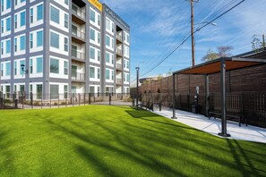A modern multi-story building with balconies, a well-maintained grassy area, and a wooden fence. - Landing | Chic 2BD, Rooftop Lounge (Richmond)