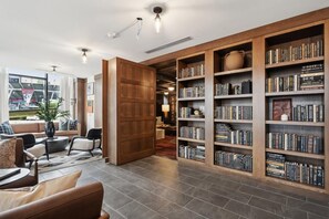 A modern library with a large bookshelf, comfortable seating, and a view of the outside. - Landing | Chic 2BD, Rooftop Lounge (Richmond)