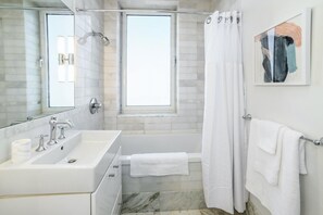 A modern bathroom with a large mirror, a sink, a bathtub, and a shower curtain. - Landing | Incredible 2BD, Pool, Gym (Roy)