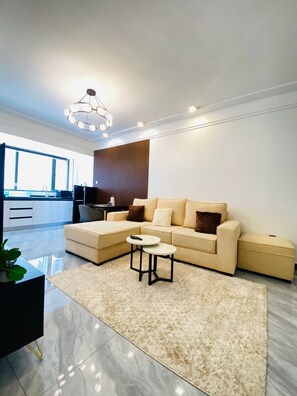 A modern living room with a sectional sofa, a small coffee table, and a large window. - Cozy 1-bedroom apartment with AC in lovely Nairobi (Nairobi)