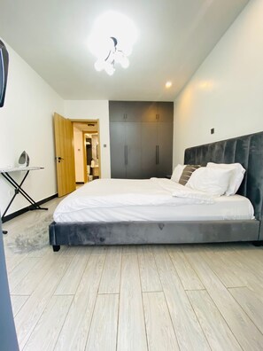 A bedroom with a bed, wardrobe, and ironing board. - Cozy 1-bedroom apartment with AC in lovely Nairobi (Nairobi)