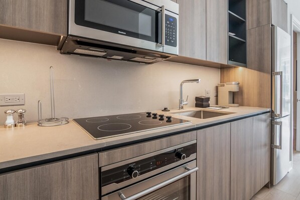 A modern kitchen with a built-in microwave, stove, oven, and a stainless steel refrigerator. - Landing | Beautiful 3BD, Gym, Pool (Roy)