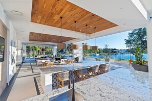 A modern outdoor dining area with a large table and chairs, a wooden ceiling, and a view of the sea. - Landing | Modern 1BD, Pool (Tampa)
