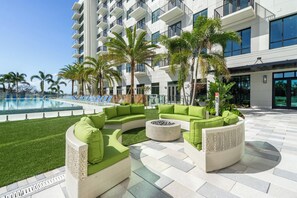 A modern outdoor seating area with green cushions, a pool, and a building with balconies. - Landing | Modern 1BD, Pool (Tampa)
