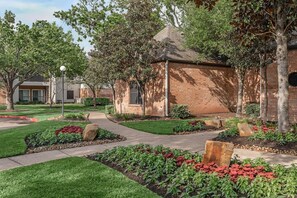 A building with a brick exterior, surrounded by a landscaped garden with a pathway, trees, and shrubs. - Landing | Stunning 1BD, Gym (Pasadena)