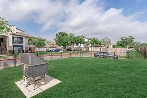 Een woonwijk met een omheinde achtertuin, een barbecue en een tweelaags gebouw met een balkon.