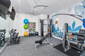 Ein Fitnessraum mit Trainingsgeräten, einer Bank und einer Wand mit Blattform-Design.
