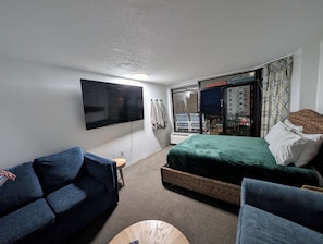 Une chambre d’hôtel dotée d’un téléviseur à écran plat fixé au mur, d’un lit recouvert d’une courtepointe verte, d’un canapé bleu et d’une petite table ronde.