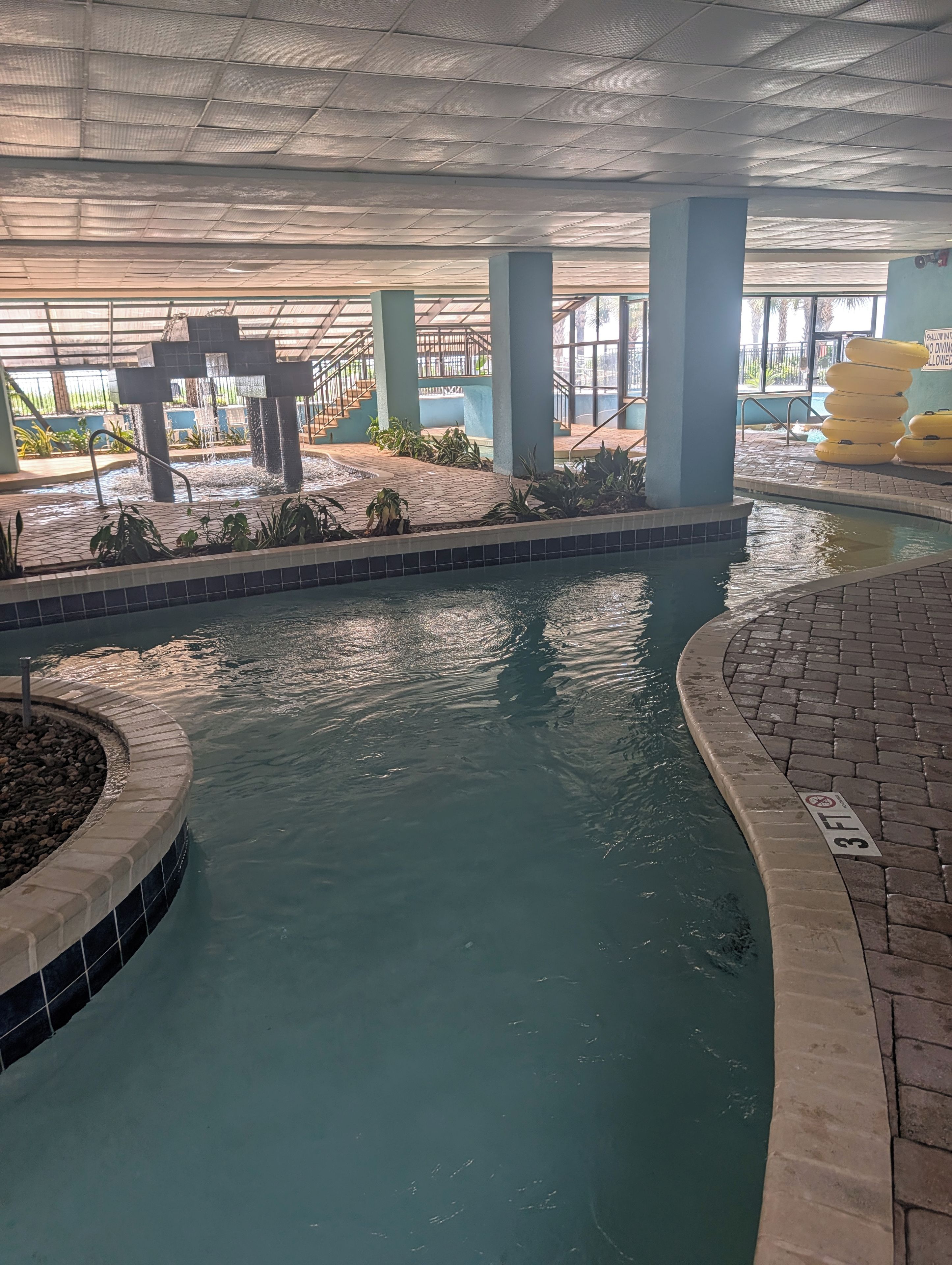 Une piscine intérieure avec un bord carrelé, une fontaine et un espace aménagé autour de la piscine, agrémenté de plantes.