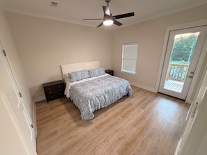 Ein Schlafzimmer mit einem Bett, einem Nachttisch, einem Deckenventilator, einem Fenster mit Jalousien und einer Tür, die auf einen Balkon führt.