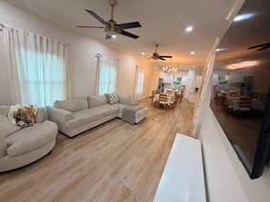 A modern living room with a sectional sofa, a dining area with a table and chairs, and a kitchen in the background. - Bay St. Louis Coastal Getaway. 3BR/3BA Near Old Town (Bay St. Louis)