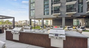 An outdoor bar area with a grill station, seating, and a view of the cityscape. - Landing | Incredible 1BD, Gym, Pool (Nashville)