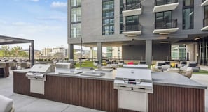 An outdoor bar area with a grill station, seating, and a view of the cityscape. - Landing | Chic 1BD, Gym, Pool (Nashville)