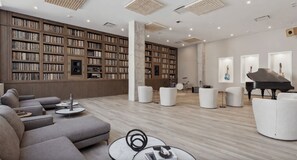A spacious library with bookshelves, a grand piano, and comfortable seating areas. - Landing | Spectacular 1BD, Pool, Gym (Nashville)