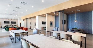 A modern office space with multiple tables and chairs, a kitchen area, and a large screen on the wall. - Landing | Incredible 2BD, Pool, Gym (Nashville)