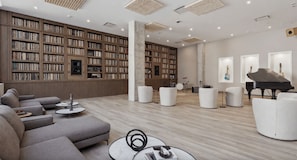 A spacious library with bookshelves, a grand piano, and comfortable seating areas. - Landing | Stunning Studio, Gym, Pool (Nashville)