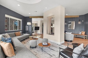 A modern living room with a grey sofa, a coffee table, and a grey armchair. There is a large window with a view of a stone wall outside. - Landing | Modern 2BD, Game Room, Clubhouse (Littleton)