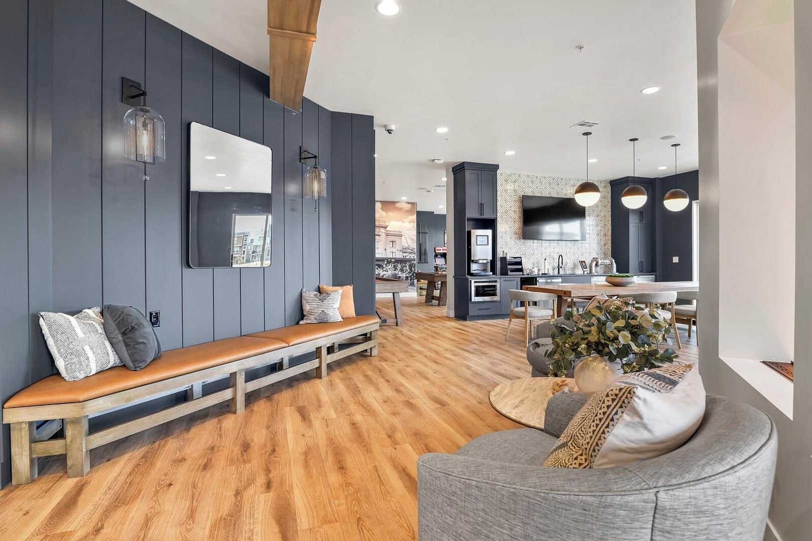 A modern living room with a wooden bench, a grey sofa, and a dining area with a table and chairs.