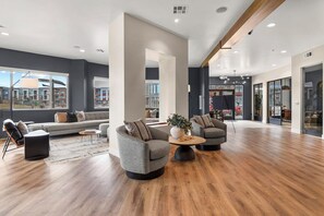 A spacious, modern lounge area with a large window offering a view of the cityscape, a wooden floor, and contemporary seating arrangements. - Landing | Incredible 2BD, Clubhouse, Game Room (Littleton)