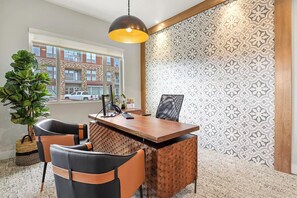 A modern office with a wooden desk, two black and orange chairs, a potted plant, and patterned wallpaper. - Landing | Modern 2BD, Game Room, Clubhouse (Littleton)