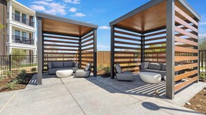 A covered outdoor seating area with a modern design, featuring a combination of wooden slats and metal beams, and a concrete floor. - Landing | Chic 1BD in Whitestone (Fort Worth)