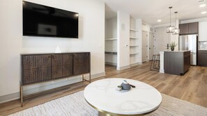 A modern living room with a flat-screen TV, a round coffee table, and a built-in cabinet. - Landing | Incredible 1BD in Whitestone (Fort Worth)