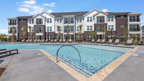 A modern apartment building with a swimming pool, lounge chairs, and a clear sky. - Landing | Incredible 1BD in Whitestone (Fort Worth)