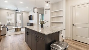 A modern kitchen with granite countertops, dark cabinetry, and pendant lighting. - Landing | Incredible 1BD in Whitestone (Fort Worth)