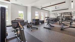Ett gym med olika typer av träningsutrustning, stora fönster och en takfläkt.