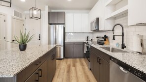 A modern kitchen with granite countertops, stainless steel appliances, and wooden cabinetry. - Landing | Modern 1BD in Whitestone (Fort Worth)