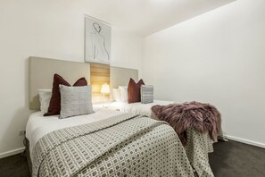 Une chambre d’hôtel comprenant un lit, une table de chevet, une lampe et une œuvre d’art accrochée au mur.