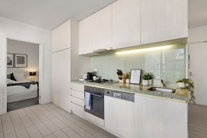 A modern kitchen with a built-in oven, a dishwasher, and a countertop with various kitchen items. - Rooftop Pool 2 Bedroom (Melbourne)