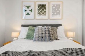 A hotel room with a bed, pillows, and three framed artworks on the wall. - Rooftop Pool 2 Bedroom (Melbourne)