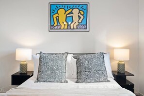 A bed with two nightstands, each with a lamp and a patterned pillow. A framed artwork is above the bed. - Unique Southbank Loft (Southbank)