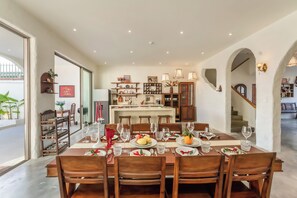 A dining area with a table set for four, wooden chairs, and a kitchen in the background. - Hidden 5BR Pool Villa - 8' Walk to An Bang Beach (Đà Nẵng)
