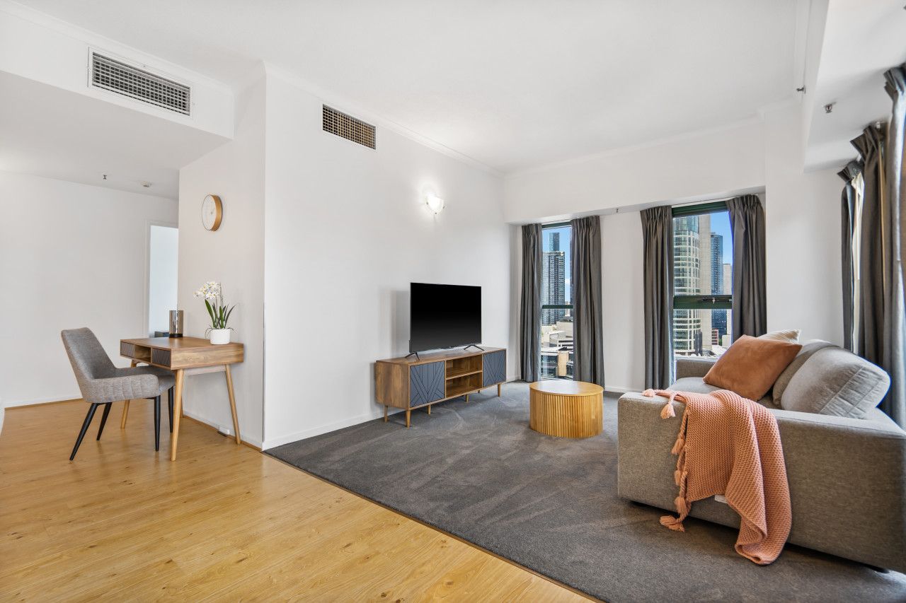 A modern living room with a sofa, a TV, a dining area with a table and chairs, and a view of a cityscape through large windows.