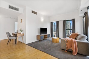 A modern living room with a sofa, a TV, a dining area with a table and chairs, and a view of a cityscape through large windows. - Yarra River View Apartment (Melbourne)