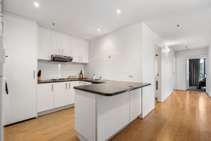 A modern kitchen with white cabinets, a central island, and wooden flooring. - Yarra River View Apartment (Melbourne)
