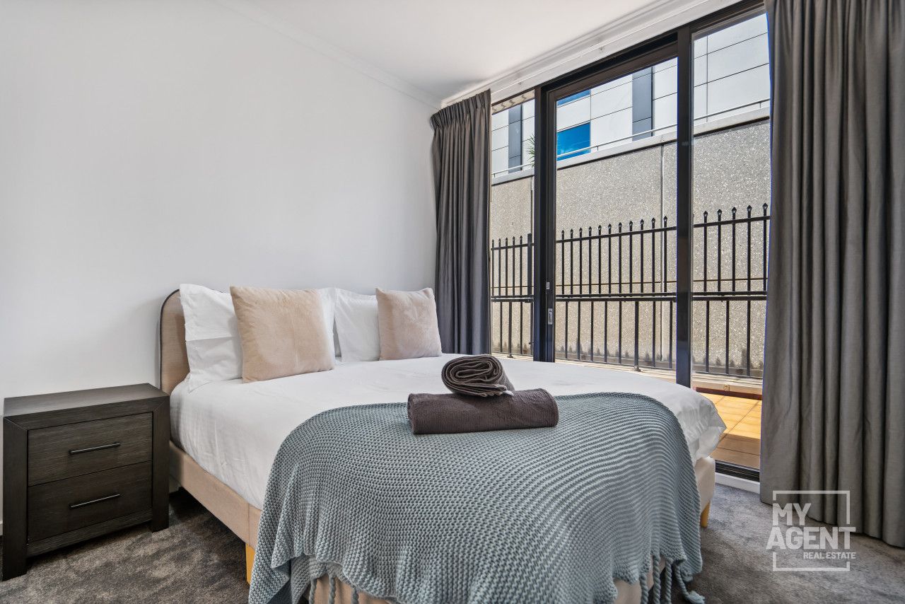 A modern hotel room with a large bed, a nightstand, and a view of a balcony with a metal fence.