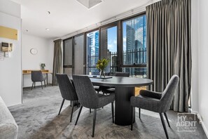 A modern conference room with a round table, grey chairs, a vase with flowers, and large windows with curtains. - Riverside Family Getaway (Melbourne)