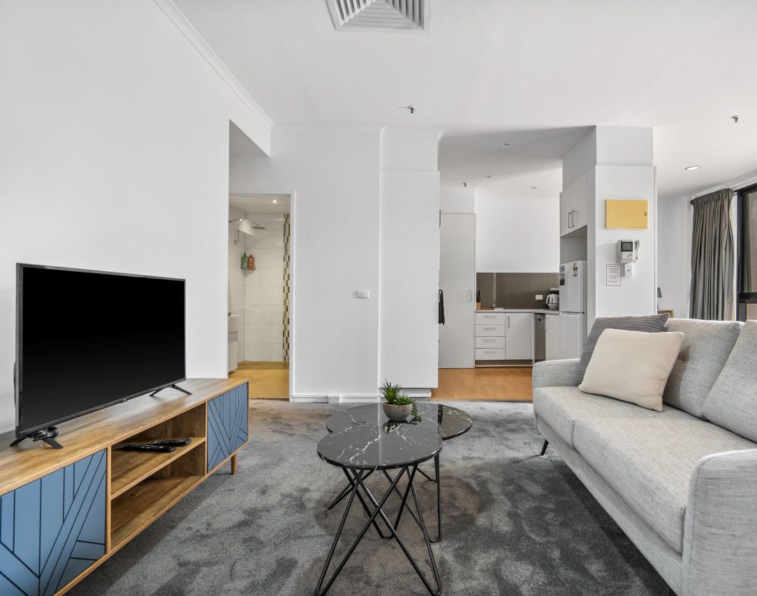 A modern living room with a flat-screen TV, grey sofa, and a small round coffee table.