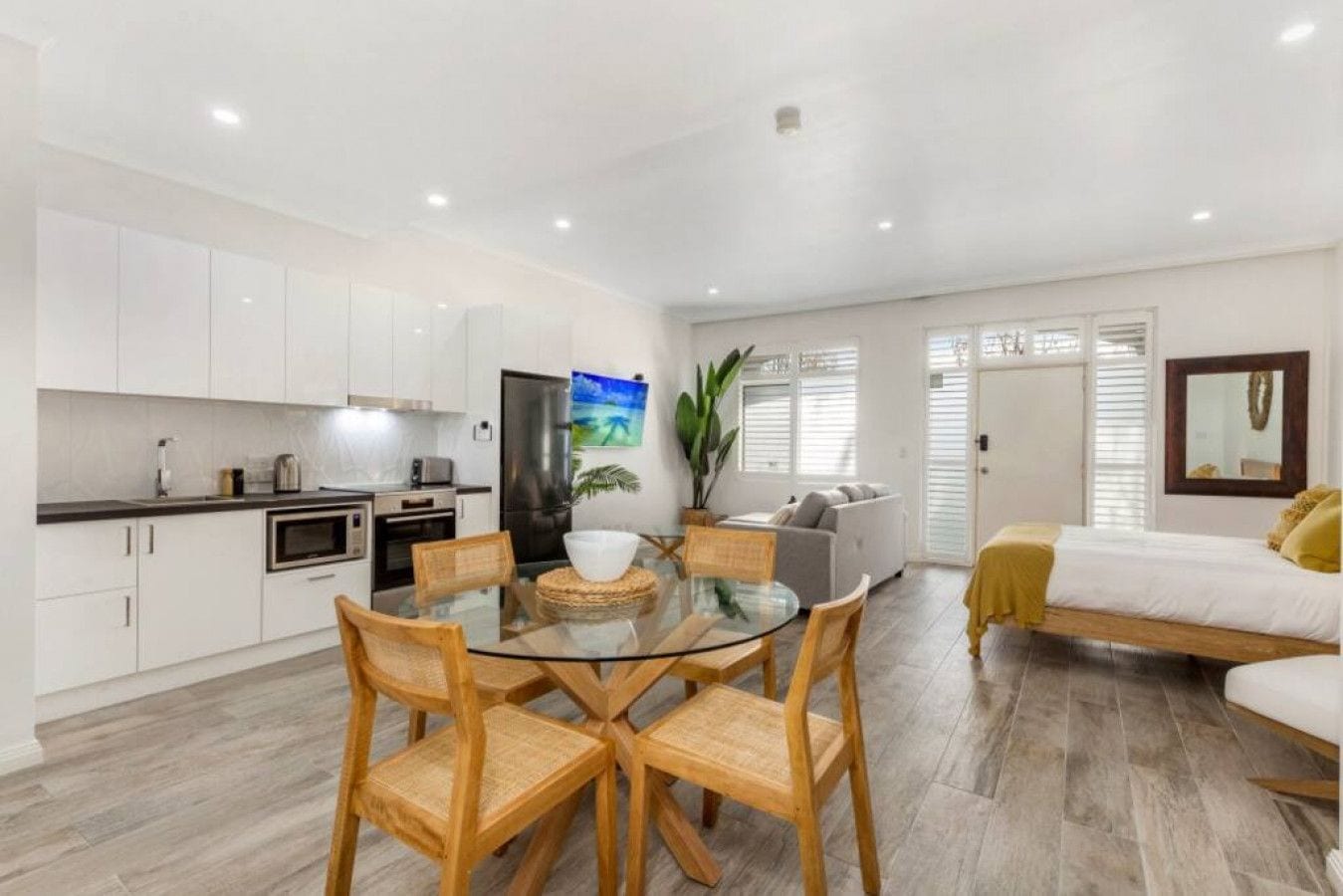 A modern kitchen with white cabinets, a dining table with chairs, and a living area with a sofa and a bed.