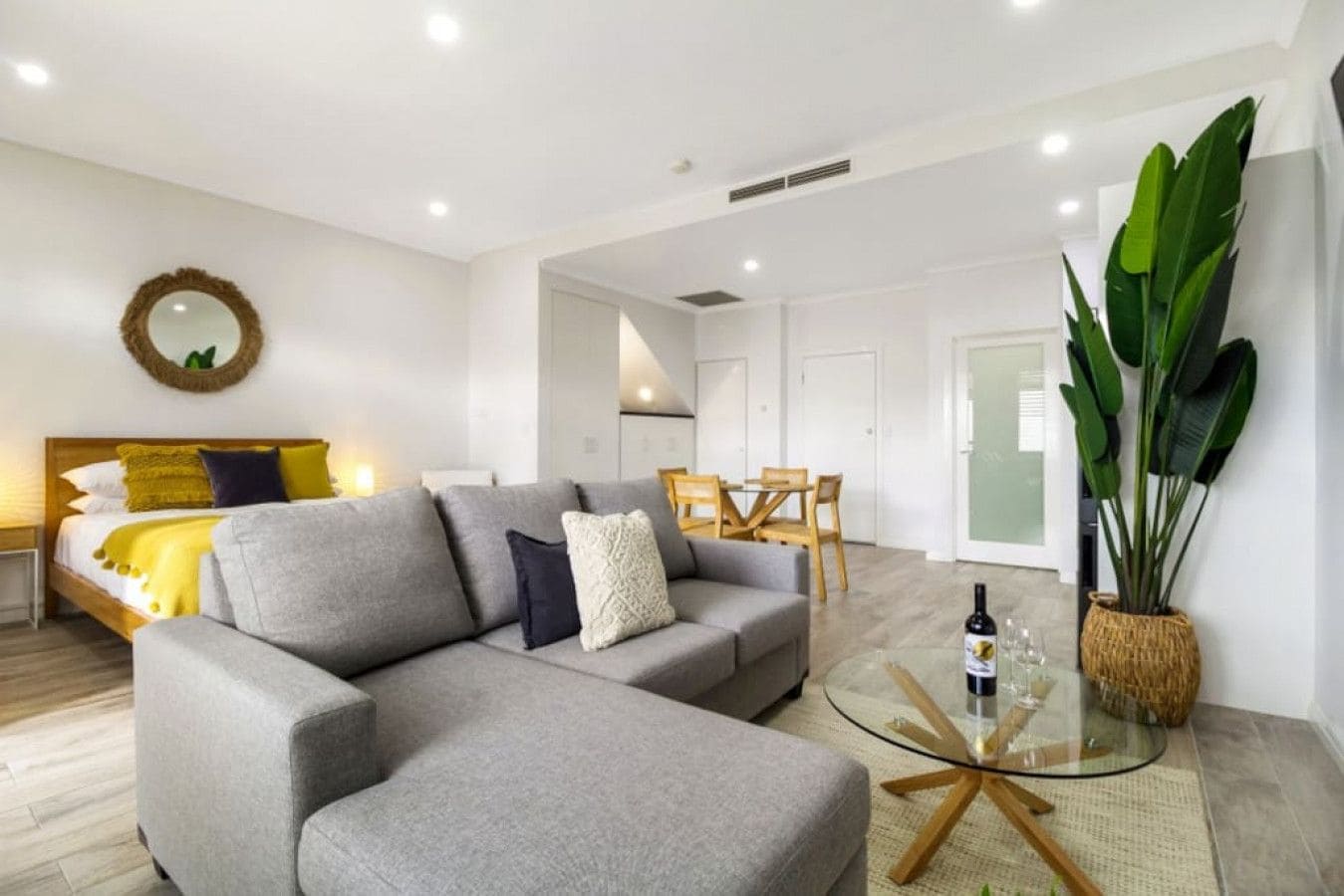 A modern living room with a grey sofa, a round coffee table, and a dining area with a wooden table and chairs.