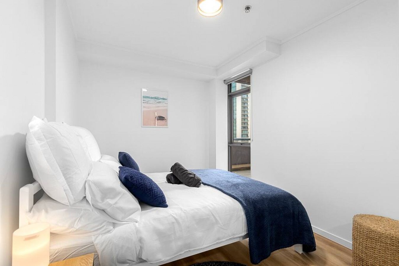 A bedroom with a bed, pillows, a blanket, a picture on the wall, and a window.