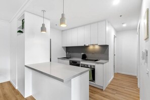 A modern kitchen with white cabinetry, a central island, and pendant lighting. - 2 Bedroom in the Paris End (Melbourne)