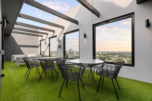 A modern interior with a round table and chairs, large windows with a city view, and a green artificial turf floor. - Vibrant Southbank 2 Bedroom (Southbank)