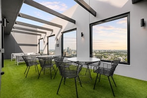 A modern interior with a round table and chairs, large windows with a city view, and a green artificial turf floor. - Luxury Southbank Skyline Stay (Southbank)