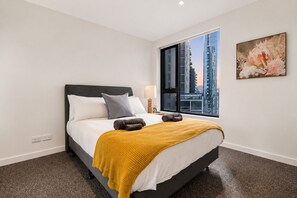 Une chambre d’hôtel moderne avec un grand lit, une fenêtre donnant sur la ville et un tableau accroché au mur.