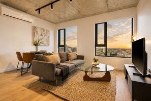 A modern living room with a sofa, coffee table, and TV, large windows with a city view, and a painting on the wall. - Luxury Southbank Skyline Stay (Southbank)