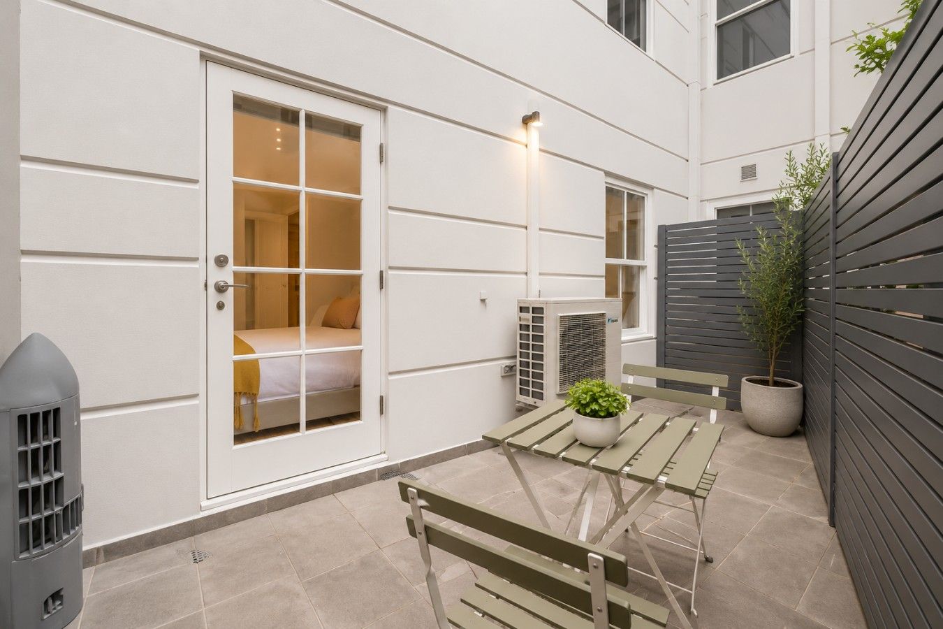 Eine moderne Terrassenausstattung mit klappbarem Tisch, einer Sitzbank, einem Blumentopf und einer Klimaanlage.